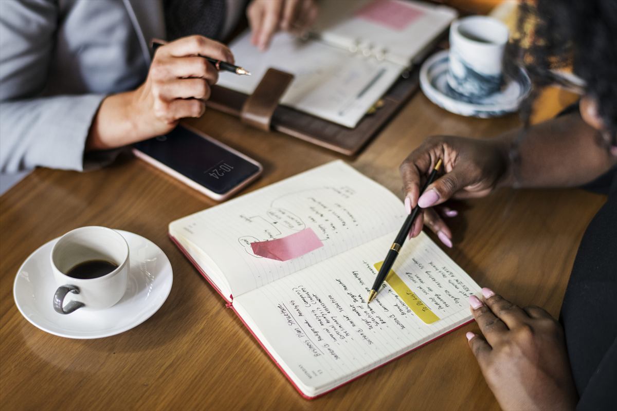 Duas pessoas conversando sobre anotações num caderno, com café