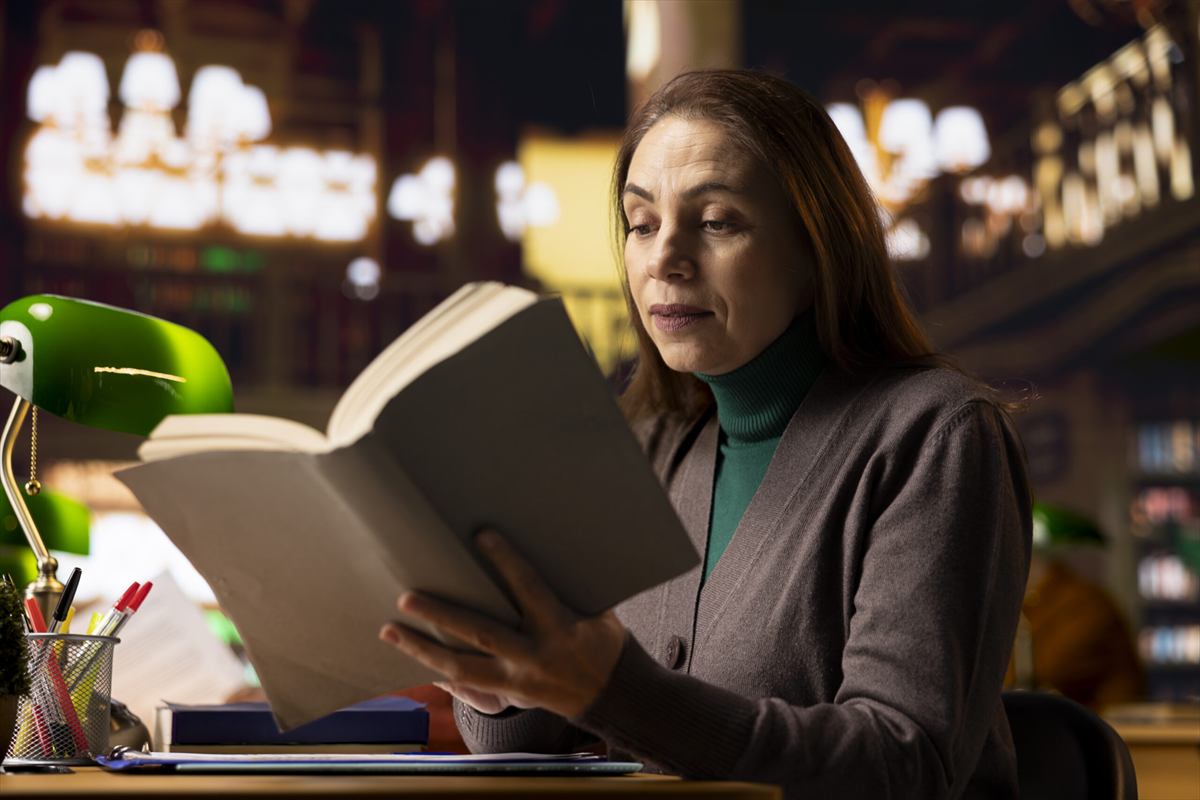 Mulher lendo um manuscrito numa mesa cheia de livros